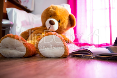 Teddy bear and book lying on wooden floor