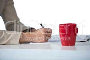 Businesswoman writing on clipboard with coffee mug on desk