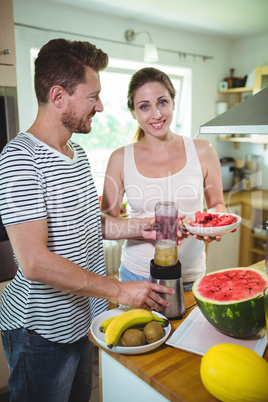 Smiling couple preparing fruit smoothie in kitchen
