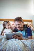 Father lying with daughter on bed and using digital tablet