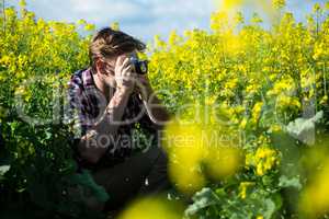 Man taking picture from camera in mustard field