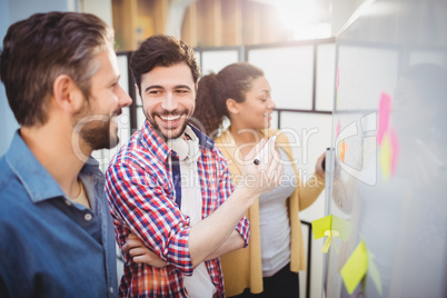 Happy executive with colleagues standing by whiteboard at creative office