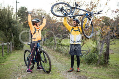 Male biker carrying mountain bike while female biker cheering him