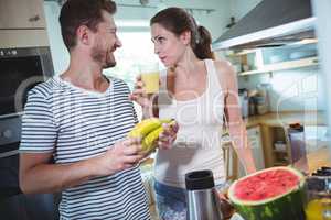 Couple holding banana and drinking smoothie in kitchen