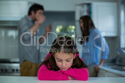 Upset girl sitting while couple having argument in background