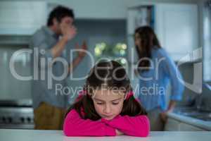 Upset girl sitting while couple having argument in background