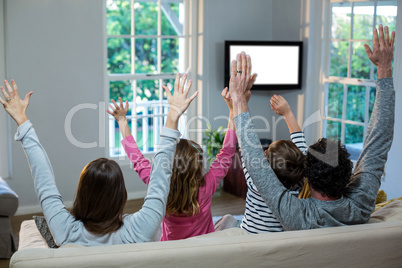 Family raising hands while watching television