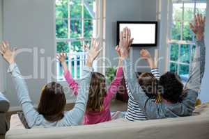 Family raising hands while watching television