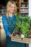 Smiling female staff holding a basket of fresh vegetables