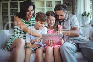 Parents sitting on sofa with their children and using digital tablet in living room