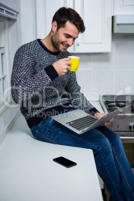 Man using laptop while having coffee in the kitchen