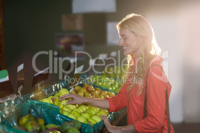 Smiling woman selecting green apples in organic section
