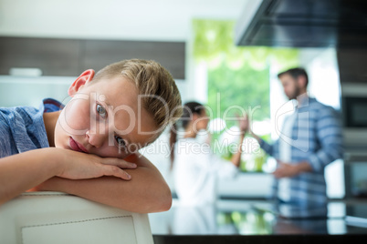 Sad boy leaning on chair while parents arguing in background