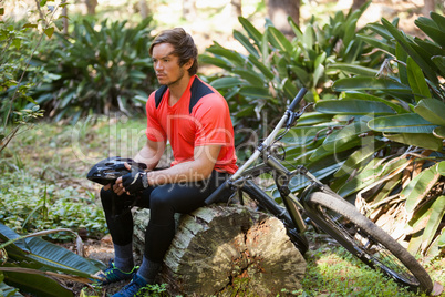 Exhausted male mountain biker relaxing on a tree trunk in the forest