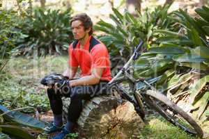 Exhausted male mountain biker relaxing on a tree trunk in the forest