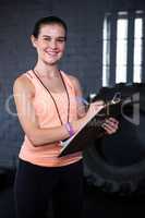 Portrait of smiling female fitness instructor writing in clipboard