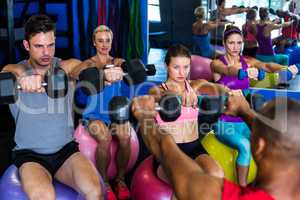 Friends holding dumbbells while sitting on exercise ball