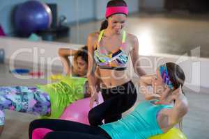 Female trainer assisting woman to exercise on exercise ball
