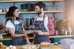 Smiling waiter and waitress using digital tablet at counter