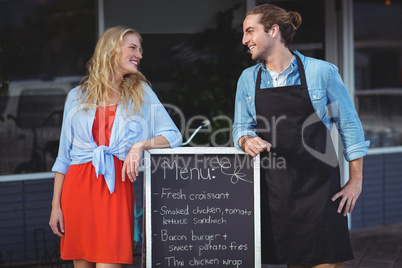 Waiter and woman standing with menu board outside the cafe