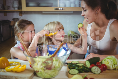 Kids feeding a slice of zucchini to mother in kitchen