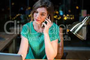 Businesswoman talking on mobile phone while working on laptop