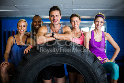 Portrait of smiling friends with tire in gym