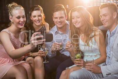 Smiling friends taking a selfie from mobile phone while having cocktail