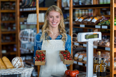 Smiling female staff holding box of cherry tomato in supermarket