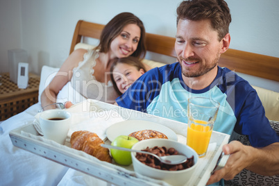 Father holding tray with breakfast on bed