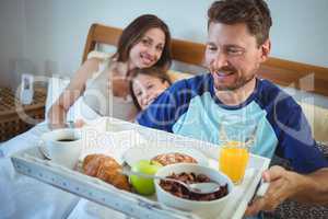 Father holding tray with breakfast on bed