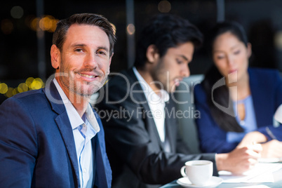 Businessman smiling at camera while colleagues interacting in the background