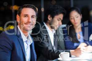 Businessman smiling at camera while colleagues interacting in the background