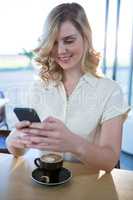 Woman using mobile phone with cup of coffee in table