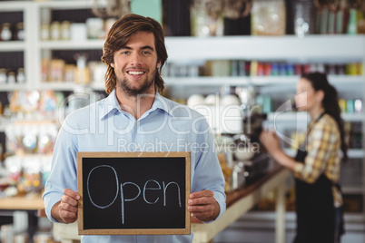 Portrait of waiter showing chalkboard with open sign