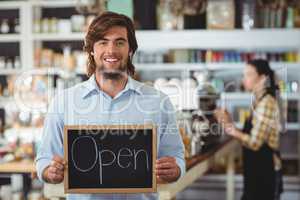 Portrait of waiter showing chalkboard with open sign