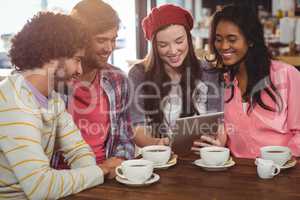 Group of friends using digital tablet while having cup of coffee