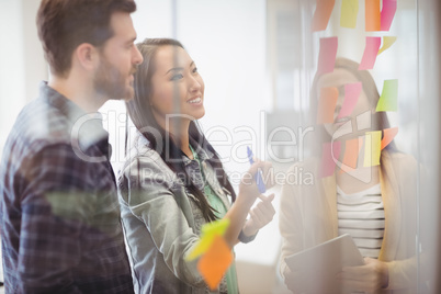 Female photo editor with coworker looking at multi colored sticky notes