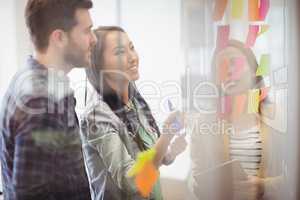 Female photo editor with coworker looking at multi colored sticky notes