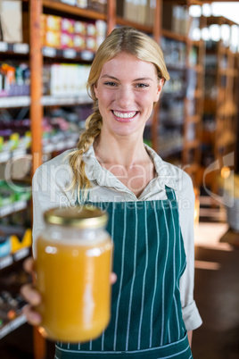 Smiling female staff holding jar of honey in supermarket