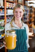 Smiling female staff holding jar of honey in supermarket