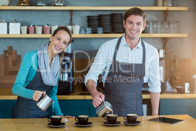 Smiling waiter and waitress making cup of coffee at counter in cafe