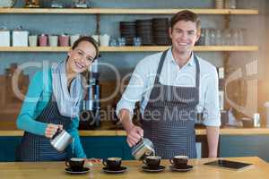 Smiling waiter and waitress making cup of coffee at counter in cafe