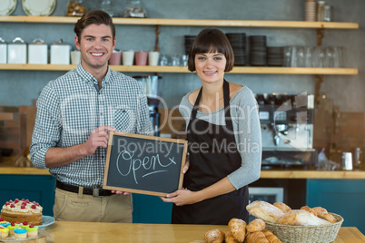Portrait of man and waitress holding slate with open sign