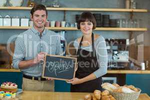 Portrait of man and waitress holding slate with open sign