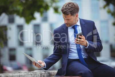 Handsome businessman holding mobile phone while using digital tablet Handsome businessman holding mobile phone while using digital tablet