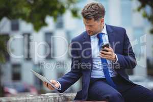 Handsome businessman holding mobile phone while using digital tablet
