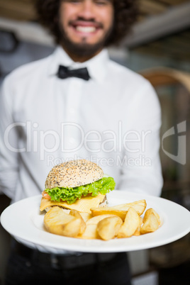 Waiter holding plates of potato chip and burger in bar