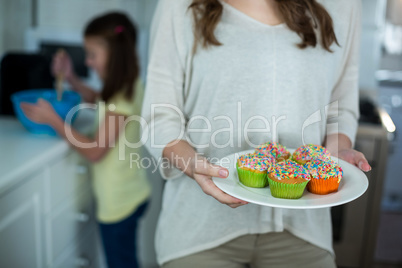 Mid-section of woman holding a plate of cupcakes