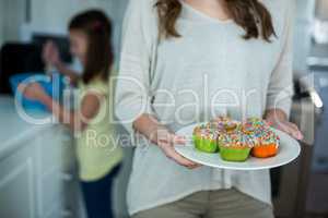 Mid-section of woman holding a plate of cupcakes